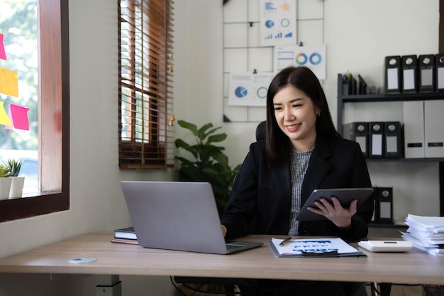 Asiatische Geschäftsfrau, die Taschenrechner und Laptop verwendet, um mathematische Finanzen auf einem Büroschreibtisch zu machen, Steuerberichte, Buchhaltungsstatistiken und analytisches Forschungskonzept