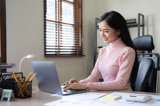 Asiatische Geschäftsfrau, die Taschenrechner und Laptop verwendet, um mathematische Finanzen auf einem Büroschreibtisch zu machen, Steuerberichte, Buchhaltungsstatistiken und analytisches Forschungskonzept