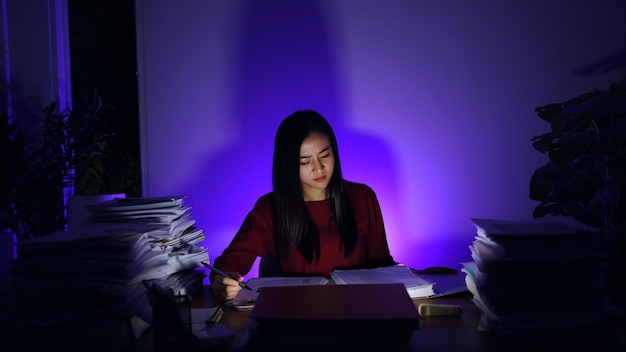 Asiatische Geschäftsfrau, die zu Hause bis spät in die Nacht mit vielen Dokumenten arbeitet. Beschäftigt und erschöpft von Überstunden in der Nacht.