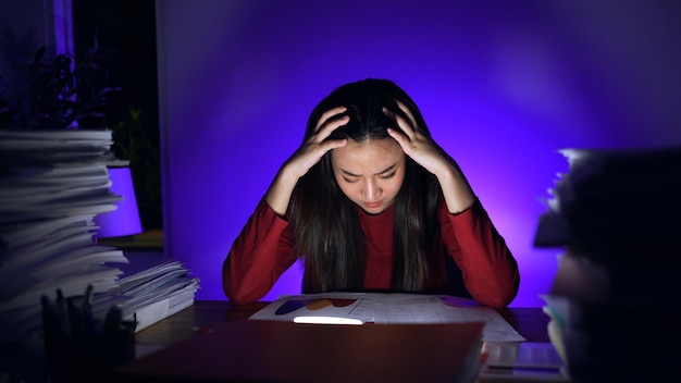 Asiatische Geschäftsfrau, die zu Hause bis spät in die Nacht mit vielen Dokumenten arbeitet. Beschäftigt und erschöpft von Überstunden in der Nacht.