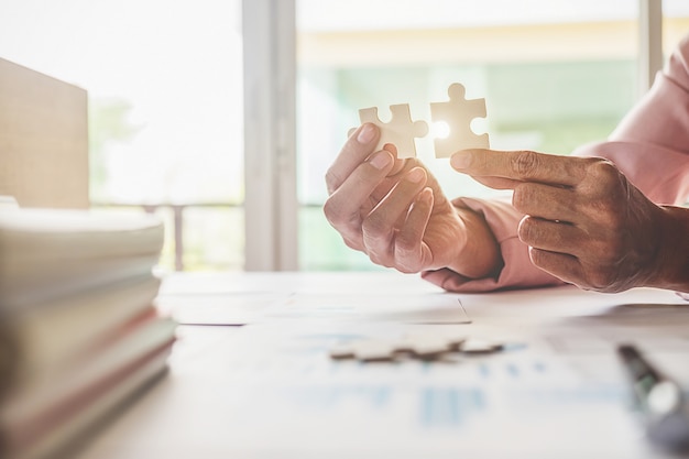 Asiatische geschäftsfrau hände auf einem hölzernen schreibtisch picken puzzle. geschäftslösungen erfolgs- und strategiekonzept. geschäftsmann hand puzzle verbinden. nahaufnahme foto mit selektiven fokus.