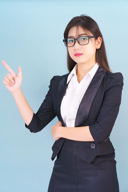 Foto asiatische geschäftsfrau in anzug mit dem finger, der auf den blauen hintergrund zeigt