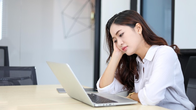 Asiatische Geschäftsfrau ist gestresst und hat Kopfschmerzen wegen ihrer Arbeit in ihrem Büro mit einem Notizbuch auf ihrem Schreibtisch