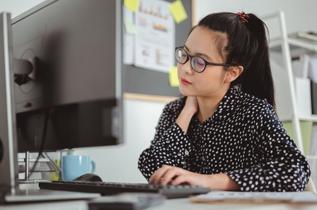 Asiatische Geschäftsfrau verspürt Nackenschmerzen, nachdem sie lange Zeit an einem Computer gearbeitet hat