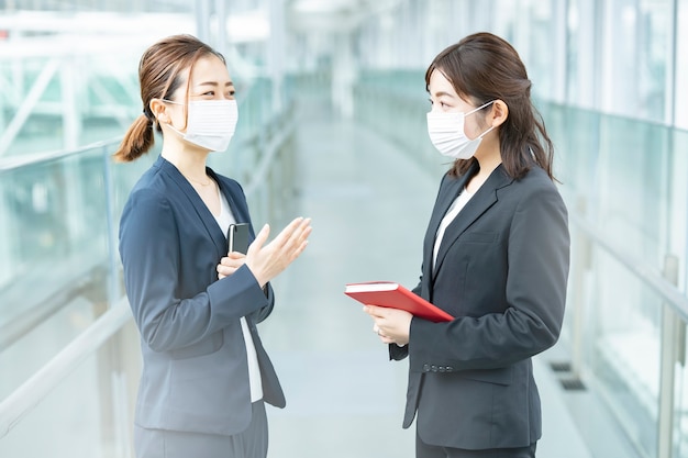 Asiatische Geschäftsfrauen, die eine Maske tragen und im Geschäftsgebäude sprechen