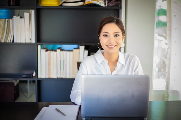 Asiatische Geschäftsfrauen, die Notizbuch verwenden und für das Arbeiten glücklich lächeln