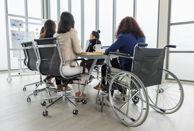 Asiatische Geschäftsfrauen und behinderte Frauen, die im Rollstuhl sitzen, treffen sich auf dem Tisch im Büro. Konzept für Geschäftstreffen.