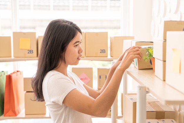 Asiatische Geschäftsinhaberin, die zu Hause mit Packbox am Arbeitsplatz arbeitet