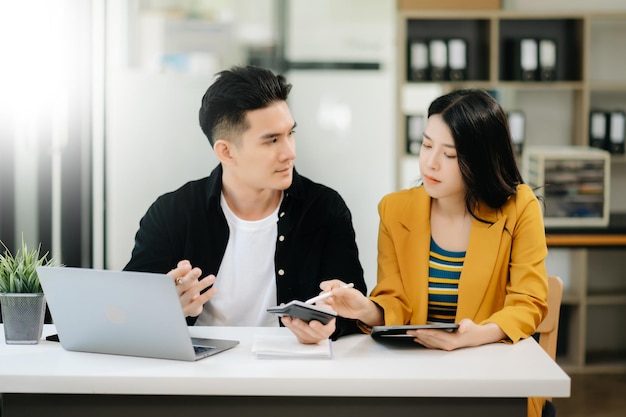 Asiatische Geschäftskollegen präsentieren und erklären Geschäfte und benutzen Laptop und Tablet Teamwork Finanzmarketing-Team, während sie in einem modernen Büroraum sitzen