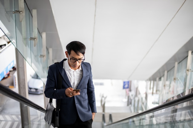 Asiatische Geschäftsleute benutzen ihre Telefone und gehen morgens die Rolltreppe hinauf, um zu arbeiten.