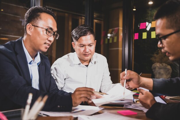 Asiatische Geschäftsmänner, welche die Arbeit sitzt im Bürokonferenzsaal an der Nachtszene besprechen