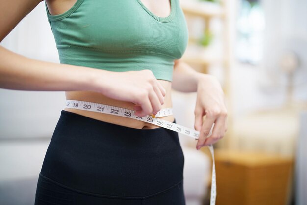 Foto asiatische gesunde frau macht diät gewichtsverlust schlanke frau misst taille mit maßband nach diät zu hause gewichtskontrolle