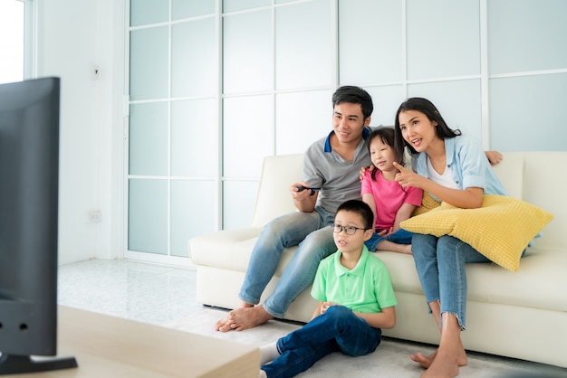 Asiatische glückliche Familie, die im Sofa sitzt und zu Hause fernsieht