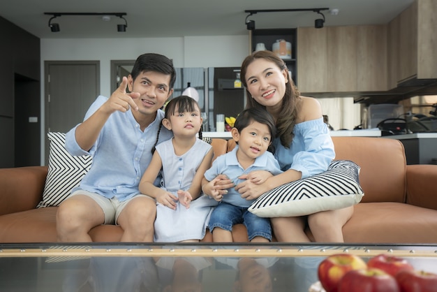 Asiatische glückliche Familie, die im Wohnzimmer zu Hause sitzt und fernsieht und eine gute Zeit zusammen für Aktivitäten am Urlaubstag verbringt