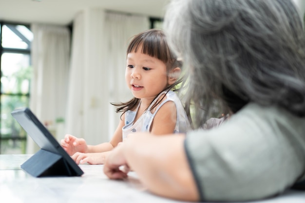 Asiatische Großmutter mit ihren beiden Enkelkindern, die Spaß haben und Online-Bildungsspiele spielen