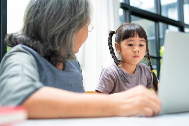 Asiatische Großmutter mit ihren beiden Enkelkindern, die Spaß haben und Online-Bildungsspiele spielen