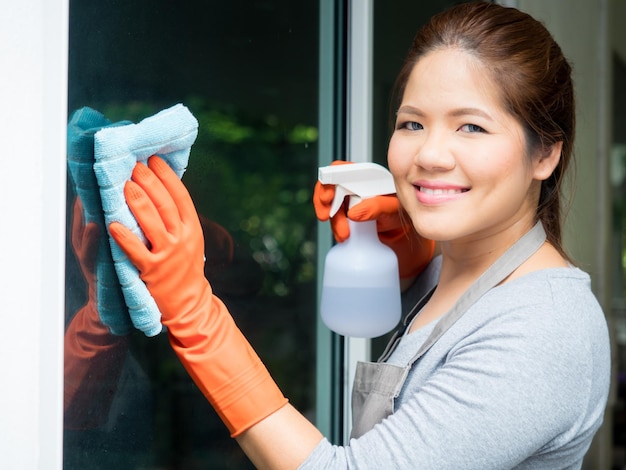 Asiatische Hausfrau putzt Fensterglas