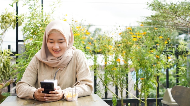Asiatische Hijab-Frau, die Telefon im Café spielt