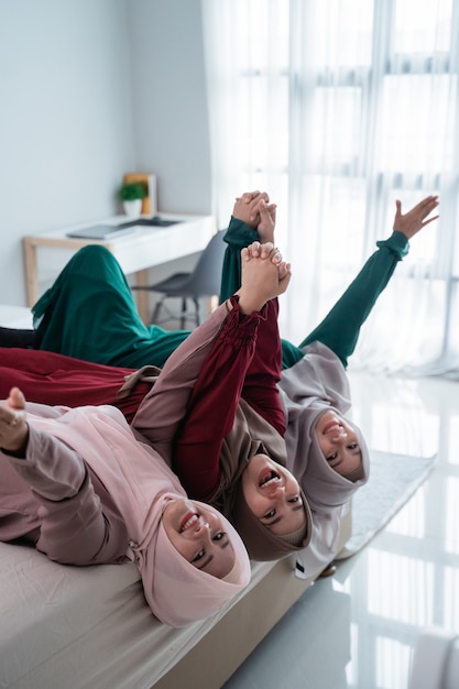 Asiatische Hijab-Frauen und -Freunde legten sich hin und hoben die Hände auf das Bett, während sie gemeinsam Spaß hatten