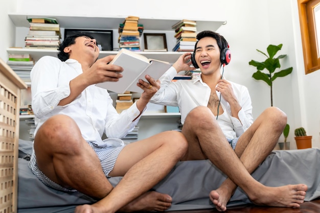 Asiatische homosexuelle Paare lachen und hören Musik, die im Hauptwohnzimmer sitzt