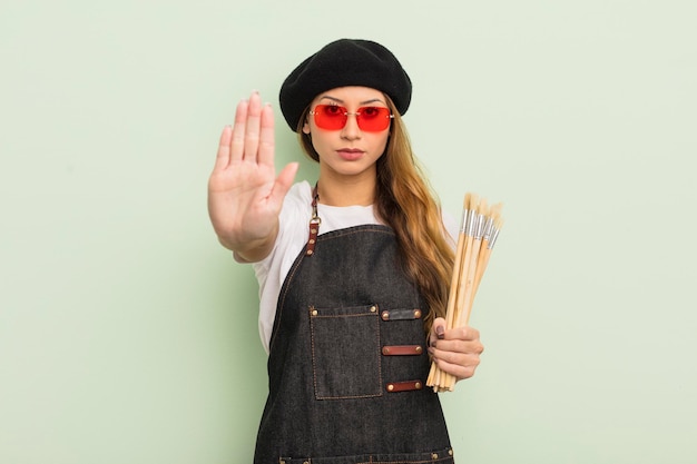 Asiatische hübsche Frau, die ernst schaut und offene Handfläche zeigt, die Stoppgesten-Künstlerkonzept macht