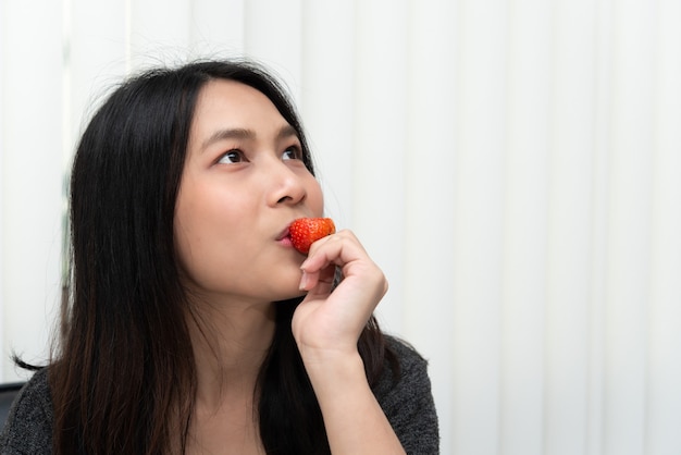 Asiatische hübsche Frau, die frische Erdbeere hält und isst