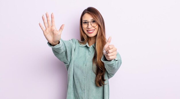 Asiatische hübsche Frau, die lächelt und freundlich aussieht und Nummer sechs oder sechs zeigt, wobei die Hand nach unten zählt