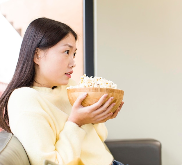 Asiatische hübsche Frau, die Popcorn isst und zu Hause einen Film anschaut