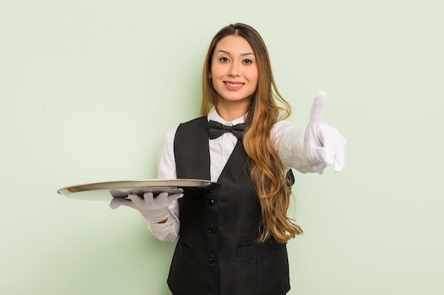 Asiatische hübsche Frau, die stolz und selbstbewusst lächelt und das Kellner- und Tablettkonzept Nummer eins macht