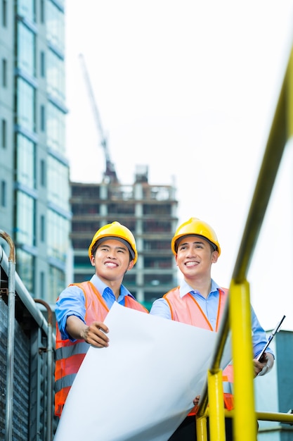 Asiatische indonesische Bauarbeiter mit Blaupause oder Plan auf der Baustelle