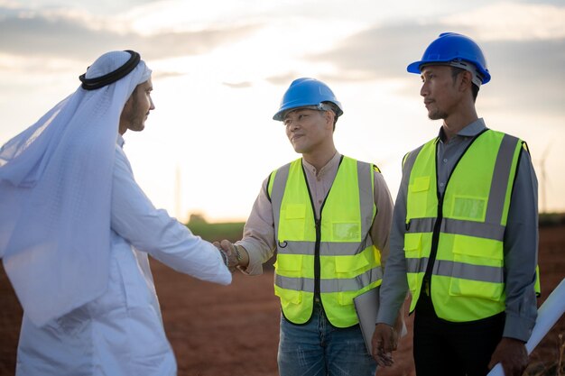 Asiatische Ingenieure und arabischer Geschäftsmann prüfen und inspizieren den Bau mit Menschen bei Sonnenuntergang am Himmel Windkraftanlage für saubere Energie und Umwelt Industriell nachhaltig