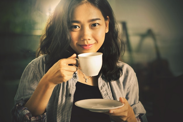 Asiatische jüngere Frau, die heißen Kaffee in der weißen Schale trinkt