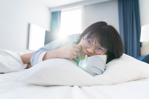 Asiatische junge Brillenfrau liegt morgens auf der Seite auf dem Bett