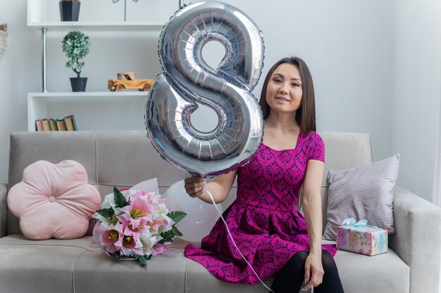 asiatische junge Frau, die Ballon Nummer acht hält, der auf einer Couch sitzt