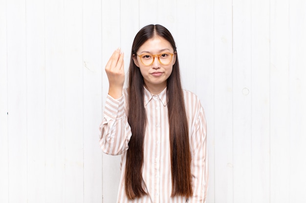 asiatische junge Frau, die Capice oder Geldgeste macht und Ihnen sagt, Sie sollen Ihre Schulden bezahlen!