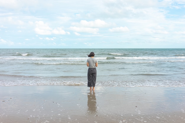 Asiatische junge frau, die das meer gegenüberstellend steht. ich fühle mich wirklich einsam, seelenruhig