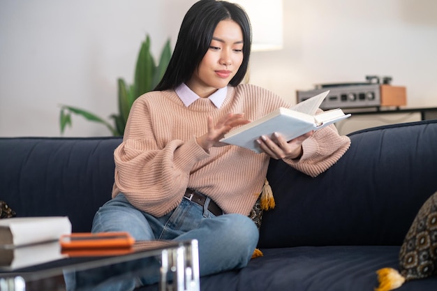 Asiatische junge Frau, die ein Buch liest und beteiligt aussieht