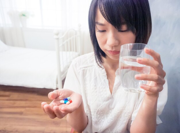 Asiatische junge Frau, die ein Glas Wasser und Pillen hält.