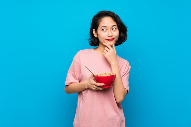 Asiatische junge Frau, die eine Schüssel Getreide eine Idee denkend hält