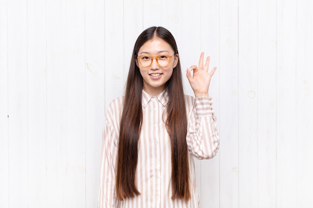 Asiatische junge Frau, die glücklich, entspannt und zufrieden fühlt, Zustimmung mit okay Geste zeigt, lächelnd