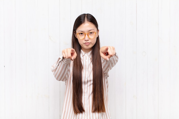 Asiatische junge Frau, die mit beiden Fingern vorwärts auf Kamera zeigt