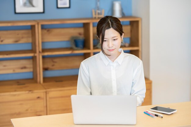 Asiatische junge Frau, die mit Laptop in einem lässigen Raum arbeitet