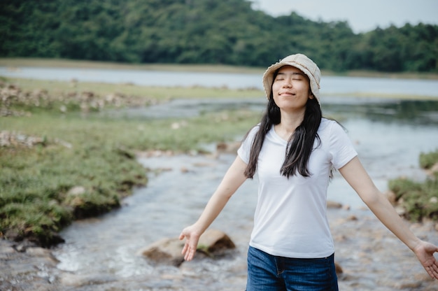 Asiatische junge Frau, die mit Natur, Feld des Wasserstroms, Wasserfall im Freien genießt und sich entspannt