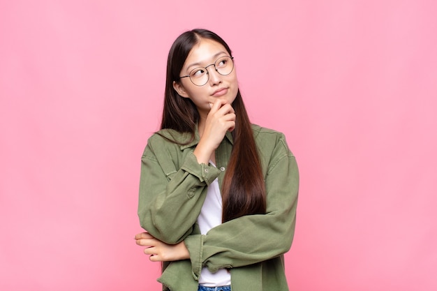 Asiatische junge Frau, die nachdenklich fühlt, sich wundert oder sich Ideen vorstellt