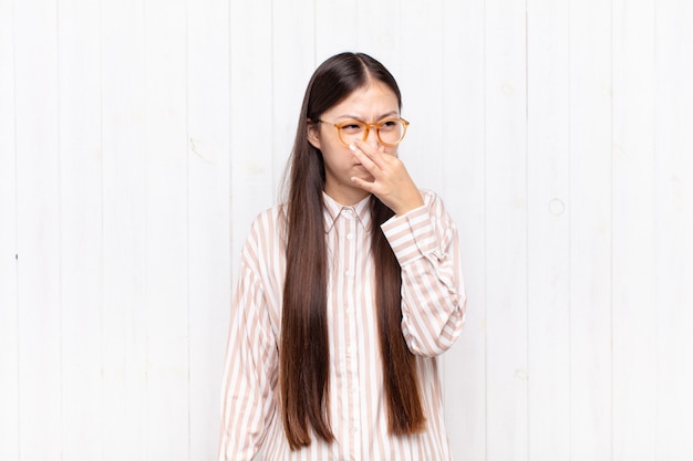 Asiatische junge Frau, die sich angewidert fühlt und die Nase hält, um einen üblen und unangenehmen Gestank zu vermeiden