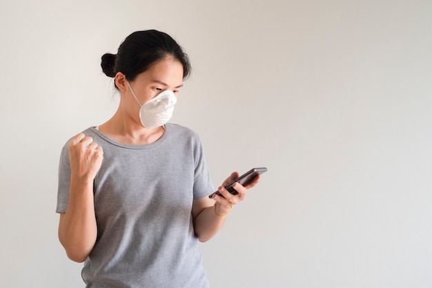 Asiatische junge Frau, die Smartphone trägt Gesichtsmaske