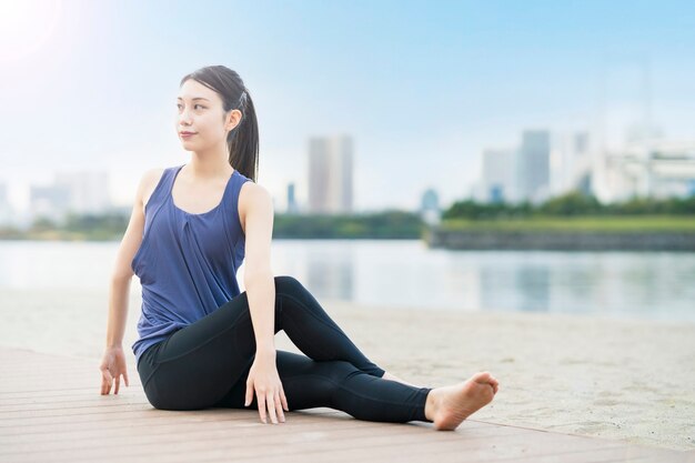 Asiatische junge Frau, die Yoga am Strand in der Stadt tut