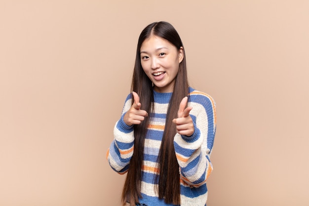 Asiatische junge Frau fühlt sich glücklich, cool, zufrieden, entspannt und erfolgreich, zeigt nach vorne und wählt Sie
