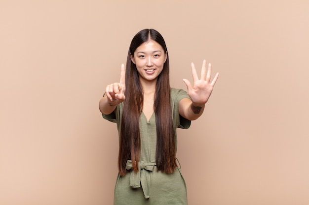 Asiatische junge Frau lächelt und sieht freundlich aus und zeigt Nummer sechs oder sechste mit der Hand nach vorne