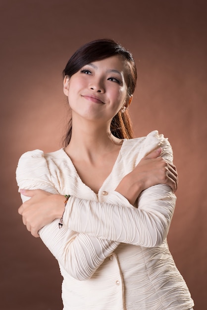 Asiatische junge Frau mit Glücksausdruck, Nahaufnahmeporträt auf braunem Hintergrund des Studios.